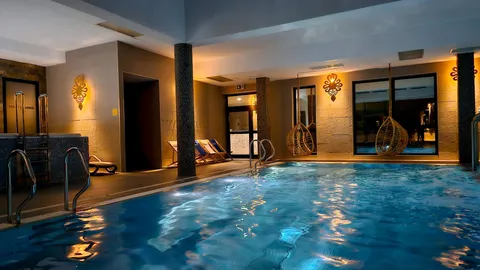 Wnętrze hali basenowej nocą z wiszącymi fotelami rattanowymi – Termy Gorce